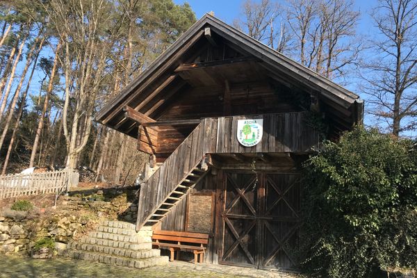 Vor hohen Bäumen und neben einem dichten Strauch steht ein rustikaler zweistöckiger Getreidespeicher aus Holz, bekannt als "Troadkasten". Unter der Außentreppe lädt eine Bank zum Rasten ein.