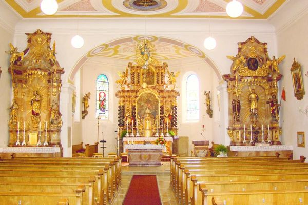 Der Innenraum der Pfarrkirche St. Jakob ist von goldenen Elementen geprägt. Zu sehen sind ein Hauptaltar und zwei Nebenaltäre, umgeben von kunstvollen Verzierungen und Dekorationen.
