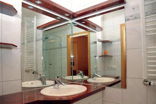 Schön renoviertes Badezimmer mit Eckspiegel, Handtuchheizkörper, Unterschrank mit eingebautem Waschbecken und roter Waschtischpatte, Wandablagen sowie einer Dusche mit Glastrennwand.