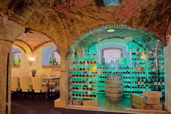 Im Gewölberestaurant steht die edle, grün beleuchtete Vinothek. Darin in der Mitte ein Holzfaß, links und rechts davor einige Weinkisten und in den Regalen lagern viele Weinflaschen.