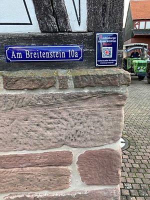 Ein historisches Haus in Amöneburg mit einem dunkelblauen Schild und QR-Code ist zu sehen.