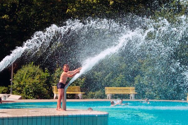Ein junger Badegast greift am Beckenrand in einen Wasserstrahl. Dieses spritzige Vergnügen entlockt ihm ein Lachen über das ganze Gesicht.