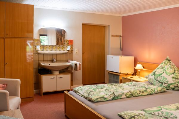 Schlafzimmer mit Bett, Waschbecken mit Spiegel, Kleiderschrank und Sitzmöbeln, beleuchtet durch Innenlicht.