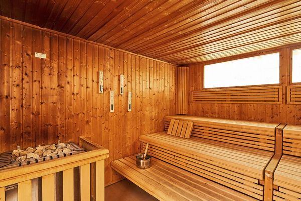 Große Sauna mit übereinanderliegenden Holzbänken, darüber befinden sich zwei Fenster. Ein Saunaofen mit Steinen ergänzt die Ausstattung.
