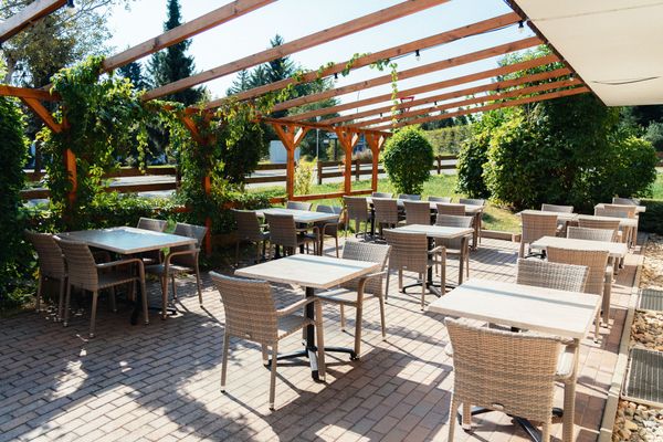 Auf dem Bild ist die Terrasse des Hotels zu sehen. Hier stehen mehrere Tische mit Stühlen unter einem Aufbau.