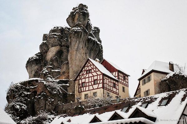 Neben einem hoch aufragenden Felsen steht ein Fachwerkhaus