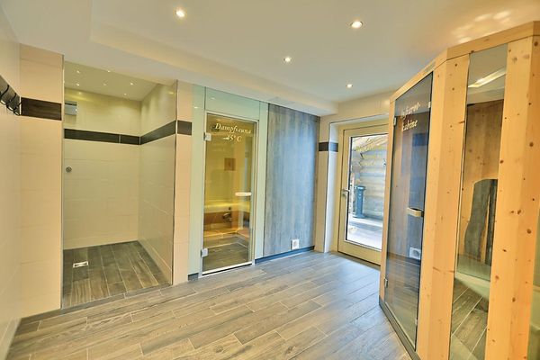 Blick auf die Dampfsauna, Infrarotkabine und den Duschbereich, durch die Tür sieht man eine Holzblocksauna