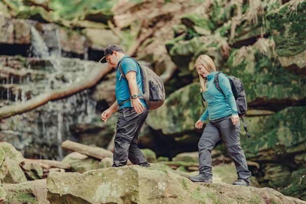 Ein Mann und eine Frau wandern durch die Margaretenschlucht, im Hintergrund ist ein kleiner Wasserfall zu sehen