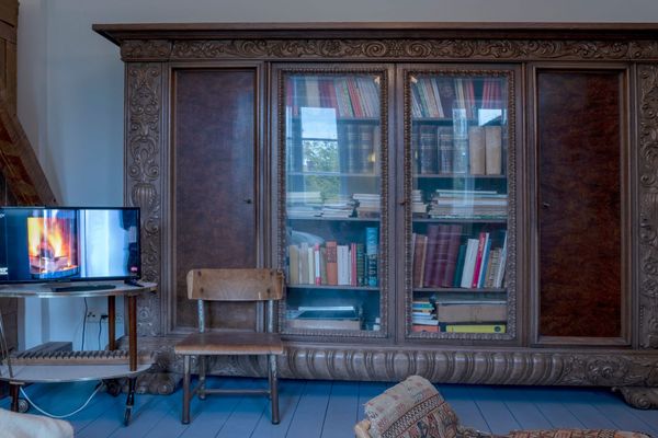 Großer verzierter Holzschrank mit Glasfächern und Büchern, daneben ein Fernseher auf kleinem Tisch und ein Holzstuhl.