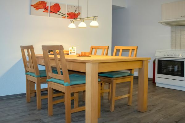 Holztisch mit vier Stühlen unter Lampe neben einer Küche mit Herd