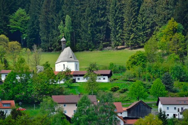 Hinter einigen Gebäuden und zwischen Sträuchern, Wald und Wiesen liegt die Leonhardikapelle, das älteste Bauwerk der Gemeinde Sankt Englmar.