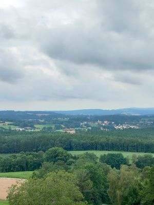 Der Blick schweift über Wiesen und Wälder zu einer Ortschaft, die eingebettet in die umgebende Natur liegt.