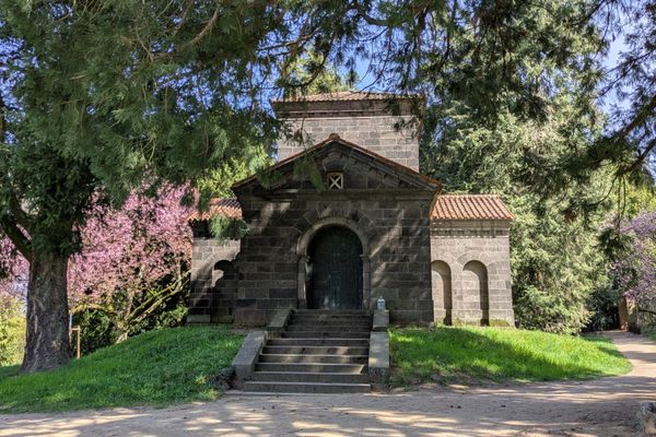 Kleines steinernes Mausoleum mit Treppe und Tür, umgeben von Bäumen und Wiese im Park