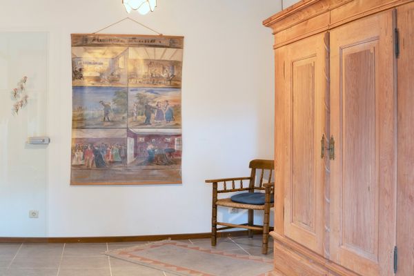Flur mit großem Holzschrank, Holzstuhl, Wandbild und Tür, Teppich auf dem Boden.