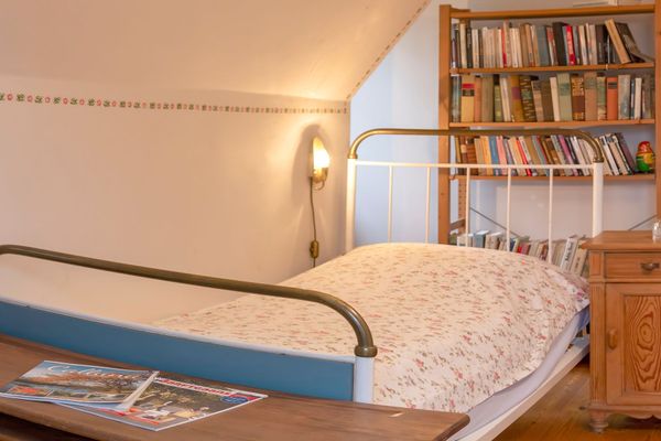 Bett mit gemusterter Bettwäsche neben einem Nachttisch und einem Bücherregal im Hintergrund.