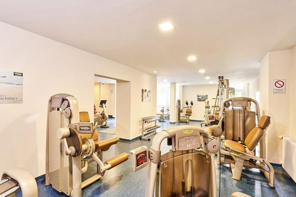 Im hellen, länglichen Fitnessraum stehen verschiedene Trainingsgeräte, darunter Kraft- und Ausdauergeräte.