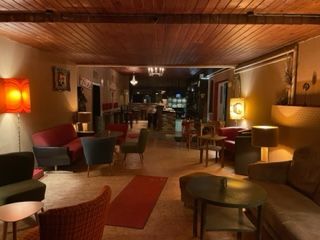 Auf dem Bild ist der Innenraum der Buntmacher´s Bar zu sehen. Auf der rechten und der linken Seite befinden sich eine Couch und verschiedene Sessel oder Stühle. Auch verschiedene Tische sind zu sehen. Die Beleuchtung ist nicht einheitlich, sowie die ganze Inneneinrichtung. Der Raum ist sehr lang (ehemalige Kegelbahn).