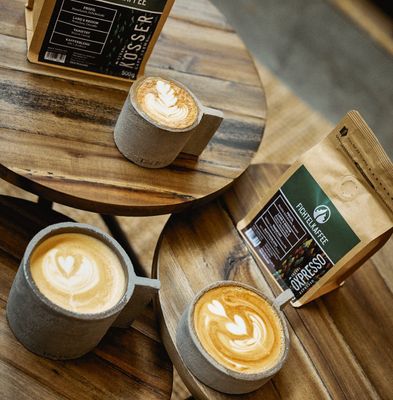 Auf dem Bild sind mehrere Tassen mit Kaffee auf Tischen stehend zu sehen. Außerdem steht eine Bohnenverpackung (Fichtelkaffee) in der Mitte.