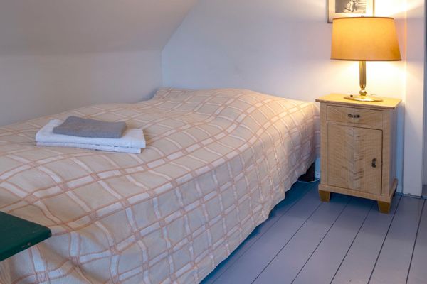 Einzelbett mit kariertem Überwurf und gefalteten Handtüchern neben einem Nachttisch mit Lampe unter einer Dachschräge.