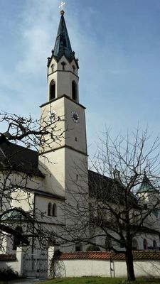 Teilansicht einer Kirche mit großem Turm, achteckigem Oberbau, Giebeln und Spitzhelm. Das Kirchengelände ist von einer Mauer umgeben