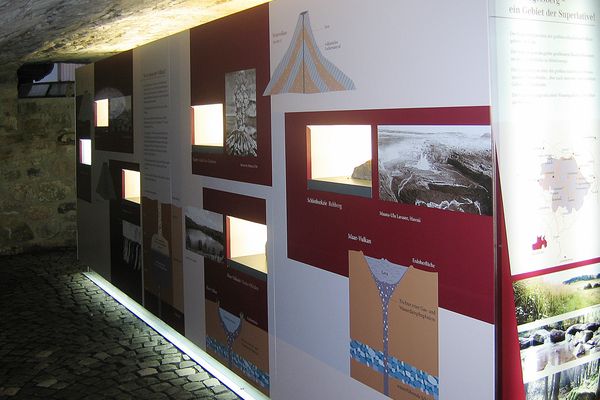 Blick in einen steinernen Gewölbekeller mit einer beleuchteten Stellwand. Hier sind Informationen über den Vulkanismus zu sehen.
