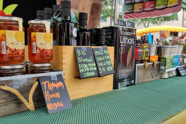 Marktstand mit Honiggläsern, Olivenölflaschen und weiteren Produkten auf grünem Tischtuch mit Preisschildern