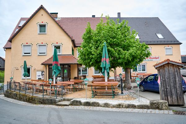 Blick auf ein Haus, vor dem ein Biergarten ist.