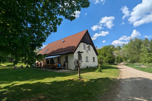 Ein kleines Haus auf einer Lichtung, an dem ein Feldweg vorbei führt.