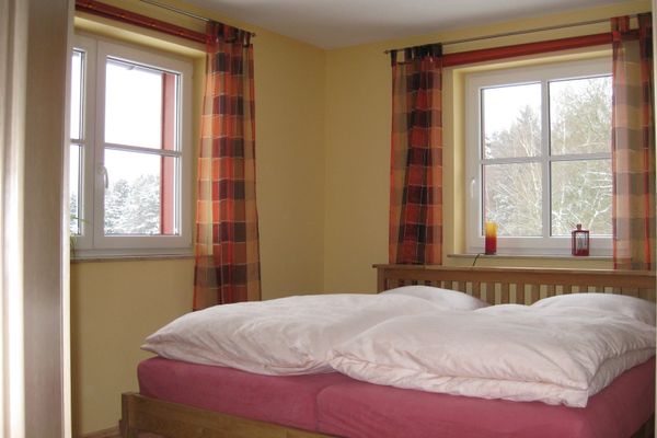 Blick in das Schlafzimmer mit großem Doppelbett und zwei Fenstern