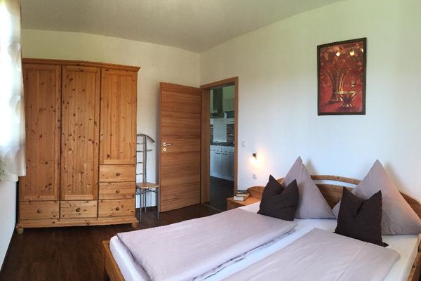 Schlafzimmer mit Doppelbett, Schrank und Garderobenstuhl. Über dem Bett hängt ein modernes Bild. Die Möbel sind aus Holz.