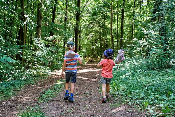 Zwei Kinder wandern mit Stock und Säckchen durch den Wald.