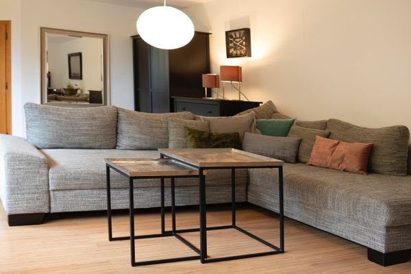 Großes graues Ecksofa mit mehreren Kissen und zwei kleinen Couchtischen davor.