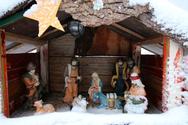 Eine weihnachtliche Krippe mit klassischen Krippenfiguren in einem kleinen Holzhaus. Am Giebel hängt ein goldener Stern.