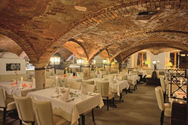 Weiße Stühle stehen vor den schön gedeckten Tischen im Gewölberestaurant. Kerzenlicht auf den Tischen erzeugen eine angenehme Atmosphäre.