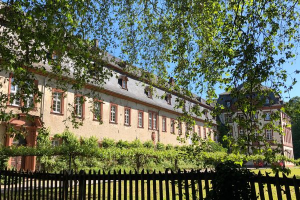 Ein Barockbau mit langgezogenem Seitenschiff steht in einer Grünanlage mit Hecken, Wiesen und Bäumen.
