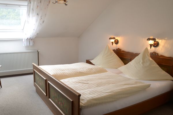 Das Bild zeigt ein Doppelzimmer mit einem Bett, an dessen Fußende Schnitzereien sind.