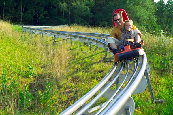 Das Bild zeigt einen Erwachsenen und ein Kind. Sie fahren auf der Sommerrodelbahn