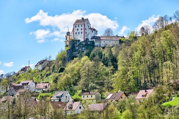 Das Bild zeigt den Ort Egloffstein mit Blick auf die Burg Egloffstein. Die Burg trohnt ganz oben auf dem Felsen, darunter schmiegen sich die bunten Häuser, teilweise aus Fachwerk in den Hang.