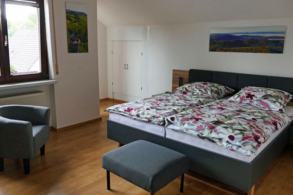 Blick in das Schlafzimmer der Ferienwohnung Hirtenberg mit Doppelbett, Sessel und Hocker