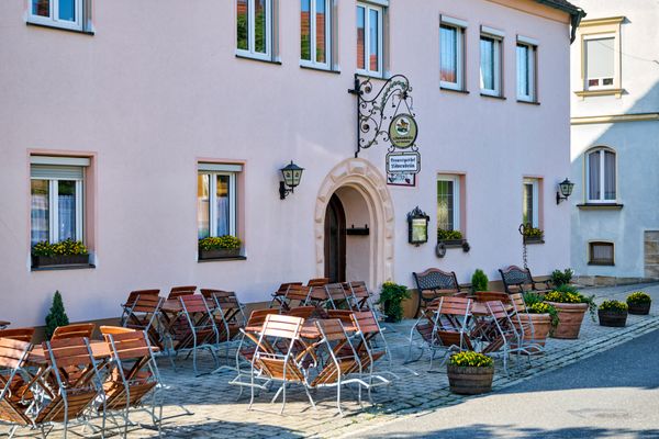 Blick auf ein rosafarbenes Haus, vor dem Tische und Stühle stehen.