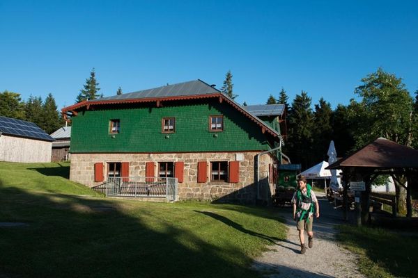 Auf dem Bild ist das Gasthaus und ein Wanderer zu sehen.