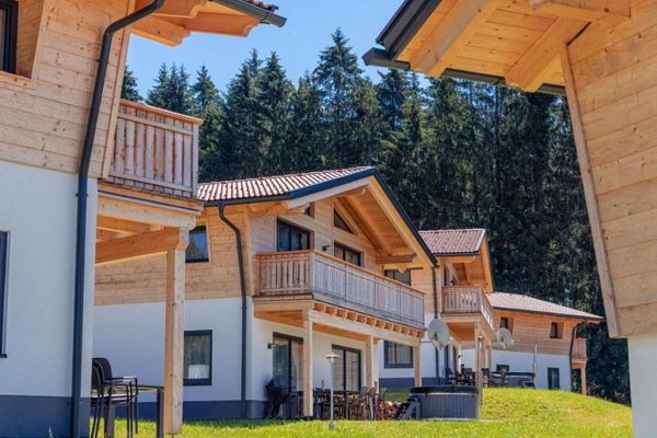 Feriendorf mit Chalets, große Balkone aus Holz, Terrasse mit Hotpot, im Hintergrund ein dichter Wald mit Nadelbäumen