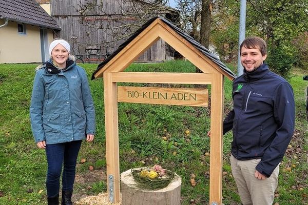 Eine Frau und ein Mann stehen neben einem Schild mit der Aufschrift Bio-Kleinladen.