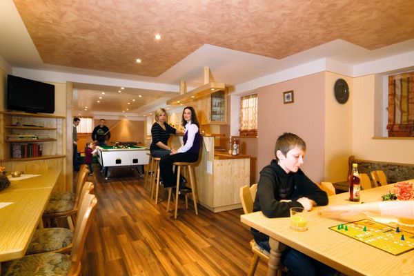 Den Party- und Spielraum nutzen Jung und Alt beim Billard, Brettspiel oder entspannt am Tresen sitzend. Bänke, Tische und Stühle bieten ausreichend Platz. Auf einem Eckschrank stehen Bücher und ein TV-Gerät.