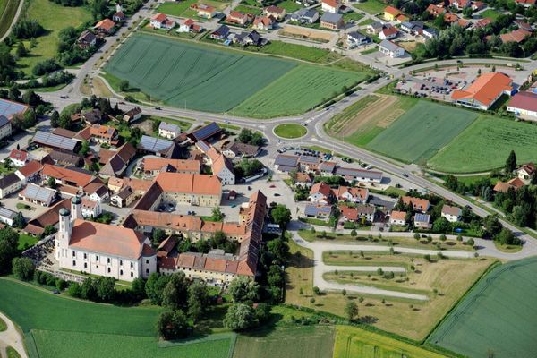 Eingebettet in Wiesen und Felder sieht man den Ort Oberalteich mit Klosteranlage und -kirche aus der Luft. Im Hintergrund erkennbar ein Teil des Ortes Furth bei Bogen und einige Einkaufsmärkte mit großem Parkplatz.