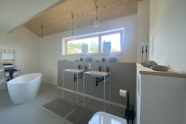 Blick in das Badezimmer mit zwei Waschbecken, freistehender Badewanne und WC