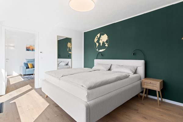 Schlafzimmer mit Doppelbett vor einer dunkelgrünen Wand