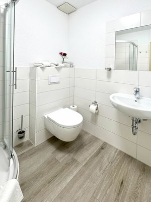 Helles Badezimmer mit gefliestem Boden, WC, Waschbecken mit Spiegel und Duschkabine.