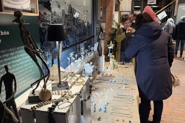 Blick auf einen Stand mit Schmuck vor einer Erklärtafel im Schlossmuseum Romrod. Drei Frauen schauen sich interessiert ein Schmuckstück an.