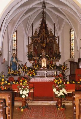 Festlich geschmückter, kleiner Altarraum unter einem Netzgewölbe. Auch ein Teil der Bankreichen, des Beichtstuhls und zwei helle, bemalte Kirchenfenster sind sichtbar.